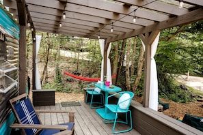 A covered outdoor area with a table and chairs, a hammock, and a view of the surrounding forest.