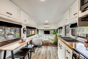 Une cuisine compacte intégrée dans un camping-car, comprenant un coin repas, un évier et une fenêtre donnant sur un jardin.