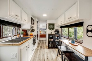 A compact kitchen with white cabinetry, a wooden countertop, a sink, and a dining area with a bench.
