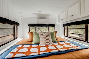 A bedroom with a large bed, multiple pillows, a window with a view, and a ceiling fan.