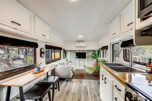 A compact RV kitchen with a dining area, a sink, and a window overlooking a garden.