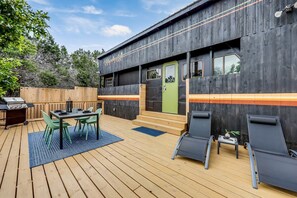 A modern outdoor deck with a wooden table and chairs, a barbecue grill, and a green door. - Unique Tiny House with Hot-tub, Fire Pit and Hiking Trail in Leander, Texas (Leander)