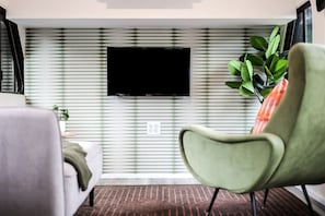 Un salon moderne avec un téléviseur à écran plat fixé sur un mur à motifs, un fauteuil vert et un canapé.