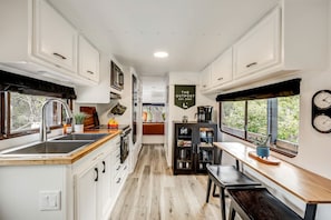 A compact kitchen with white cabinetry, a wooden countertop, a sink, and a dining area with a bench. - Unique Tiny House with Hot-tub, Fire Pit and Hiking Trail in Leander, Texas (Leander)