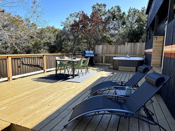 A wooden deck with a table and chairs, a hot tub, and lounge chairs. - Unique Tiny House with Hot-tub, Fire Pit and Hiking Trail in Leander, Texas (Leander)