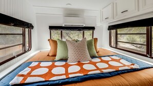 A bedroom with a large bed, multiple pillows, a window with a view, and a ceiling fan.