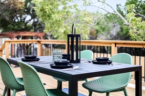 A deck with a table set for dining, surrounded by green chairs, and a railing in the background. - Unique Tiny House with Hot-tub, Fire Pit and Hiking Trail in Leander, Texas (Leander)