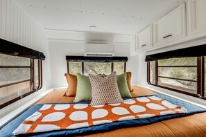A bedroom with a large bed, multiple pillows, a window with a view, and a ceiling fan.