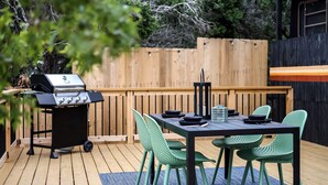 An outdoor patio with a grill, a table, and green chairs.