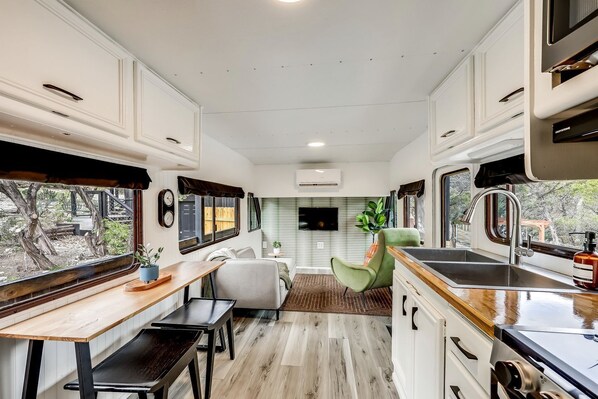 A compact RV kitchen with a dining area, a sink, and a window overlooking a garden. - Unique Tiny House with Hot-tub, Fire Pit and Hiking Trail in Leander, Texas (Leander)