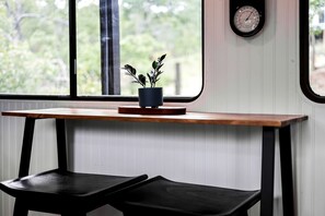 A table with a potted plant, a clock, and a bench in a room with a window.