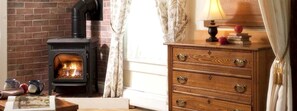 Une pièce avec un poêle à bois, une commode en bois et une lampe sur une table.