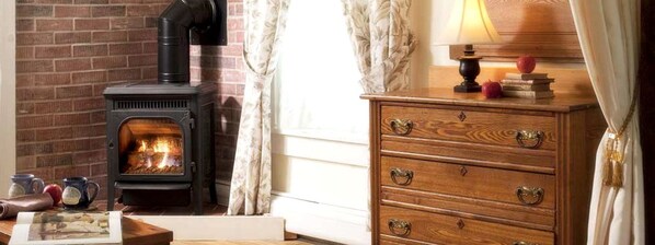 A room with a wood-burning stove, a wooden dresser, and a lamp on a table.