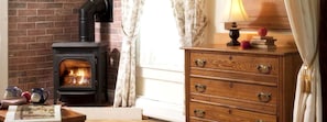 A room with a wood-burning stove, a wooden dresser, and a lamp on a table. - Bed and Breakfast Suite with Jacuzzi Bathtub in Mad River Valley of Vermont (Warren)