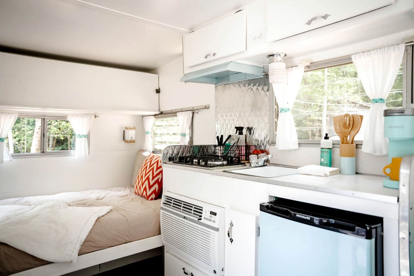 Ein kompaktes Wohnmobil-Interieur mit Bett, Küchenzeile und einem Fenster mit Vorhängen.