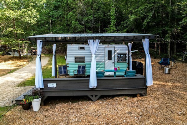 A mobile home with a porch, two chairs, a table, and a small garden area.