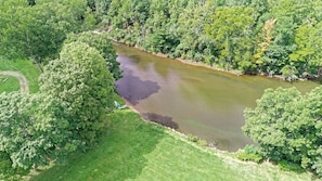 An aerial view of a river surrounded by dense greenery, with a small grassy area and a visible path.
