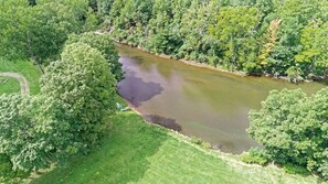 Vista aérea de un río rodeado de abundante vegetación, con un pequeño espacio cubierto de césped y un camino visible.