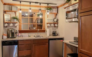 Une cuisine avec des armoires en bois, un four à micro-ondes encastré, une machine à café et des luminaires suspendus.