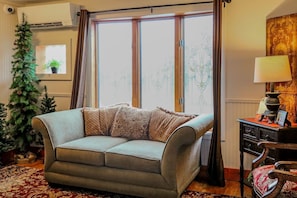A living room with a sofa, a Christmas tree, a lamp, and a window with curtains.