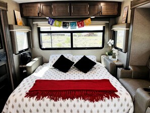 Une chambre à coucher avec un lit, des oreillers, une couverture rouge, une fenêtre, des armoires et une petite table sur laquelle se trouve une plante.