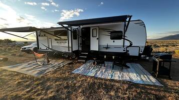 A recreational vehicle with a covered living area, a picnic table, and a grill set up in a grassy field.