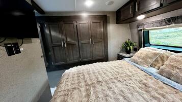A bedroom with a large bed, a wardrobe, a television, and a window with a view.
