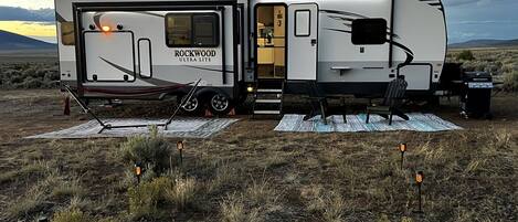 Una caravana Rockwood Ultra Lite estacionada en un campo bajo un cielo despejado.