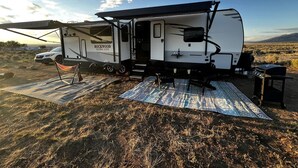 Un véhicule récréatif doté d’un espace de vie abrité, d’une table de pique-nique et d’un barbecue installés dans un champ herbeux.