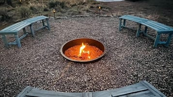 Un campeggio con un focolare, due panche e un camper sullo sfondo.