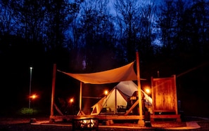 A tented camping area with a canopy, a fire pit, and a wooden structure.