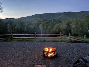 Un espace recouvert de gravier, avec un foyer, une clôture en bois et une vue sur une chaîne de montagnes boisées.