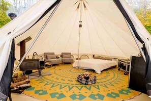 Una carpa con una cama, dos sofás, una mesita, un calentador y una alfombra.