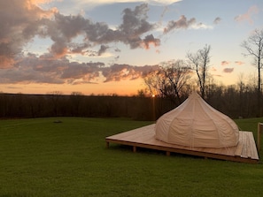 Una carpa montada en un campo cubierto de hierba con un atardecer de fondo.