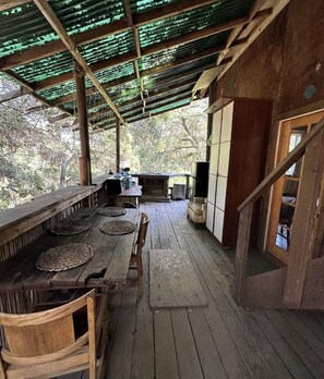 Una estructura de madera rústica con un espacio exterior cubierto, una mesa de comedor con individuales tejidos y una chimenea de piedra.