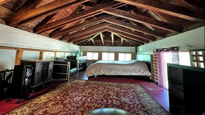 Una habitación con techo alto, vigas de madera, una cama, un televisor y una alfombra estampada.