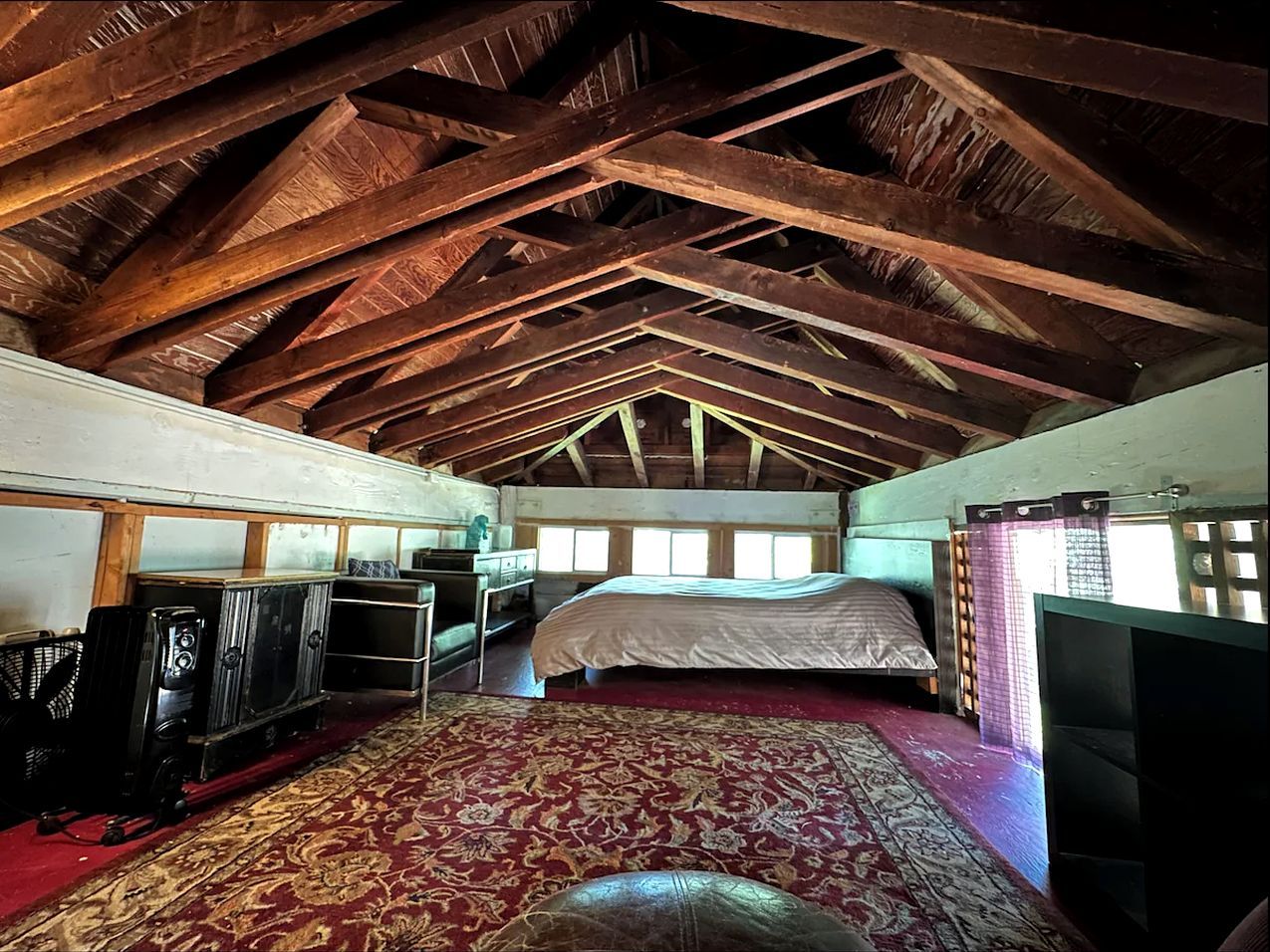 Een kamer met een hoge plafond, houten balken, een bed, een televisie en een kamerbreed tapijt met een patroon.