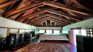 Een kamer met een hoge plafond, houten balken, een bed, een televisie en een kamerbreed tapijt met een patroon.