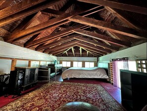 Una habitación con techo alto, vigas de madera, una cama, un televisor y una alfombra estampada.