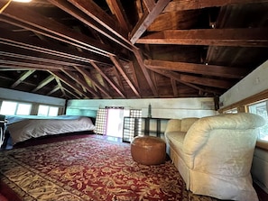 A room with a bed, a sofa, a small ottoman, a window, and a traditional Japanese shoji screen.