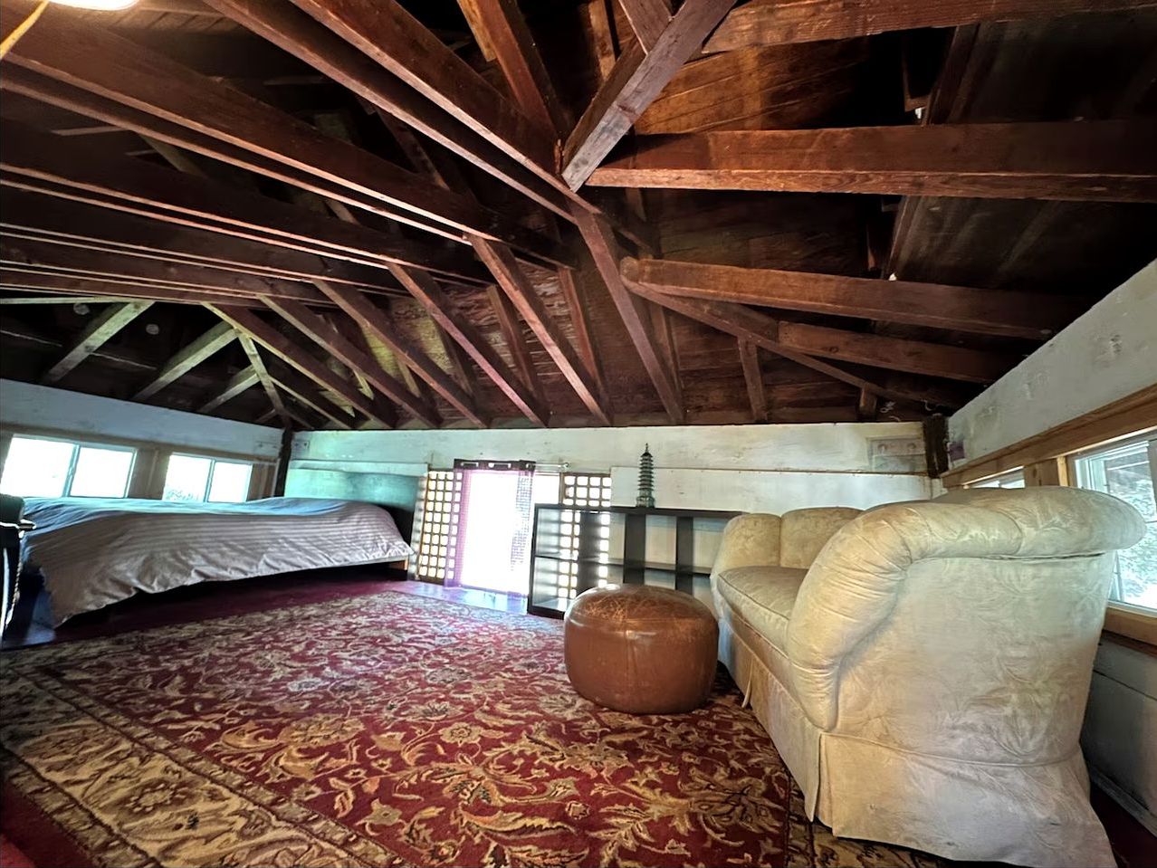 Ein Zimmer mit einem Bett, einer Schlafcouch, einem kleinen Hocker, einem Fenster und einem traditionellen japanischen Shoji-Bildschirm.