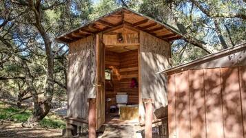 Eine Holzhütte mit geneigtem Dach, einer kleinen Veranda und einem sichtbaren Innenraum mit Bett und Fenster.