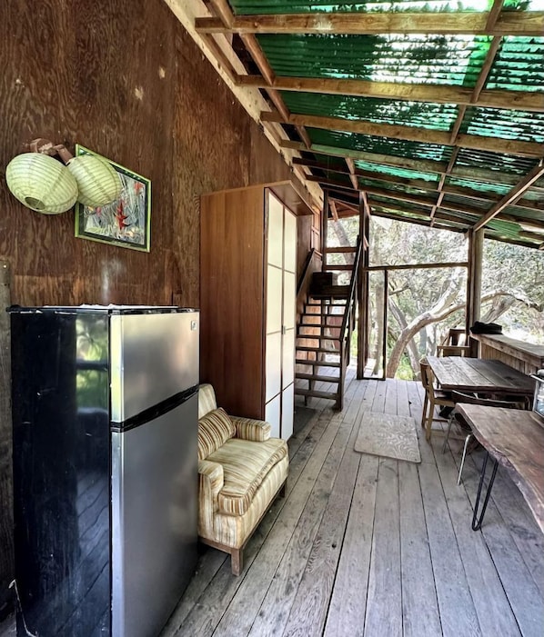 A wooden cabin with a sofa, a refrigerator, a dining table, and a staircase leading to a loft.