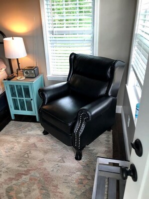 A black leather armchair with decorative studs, a teal side table with a radio, and a patterned rug.