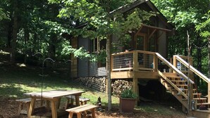 Una cabaña de madera con un porche y escaleras, rodeada de árboles.
