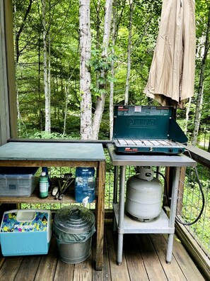 Eine Holzterrasse mit einem Propanherd, einem Wasserspender und einer Kühlbox.