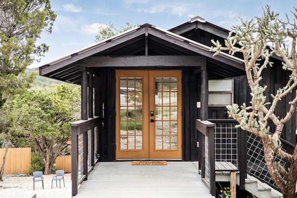 A wooden house with a porch, a double door, and a small outdoor seating area.