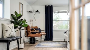 Ein modernes Wohnzimmer mit einer Ledersofa, einem Couchtisch, einer Topfpflanze und einem großen Fenster mit Vorhängen.