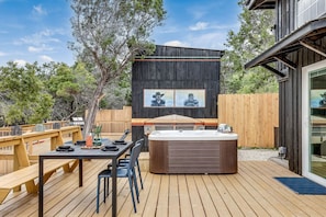 A wooden deck with a hot tub, a table with chairs, and a wooden fence.