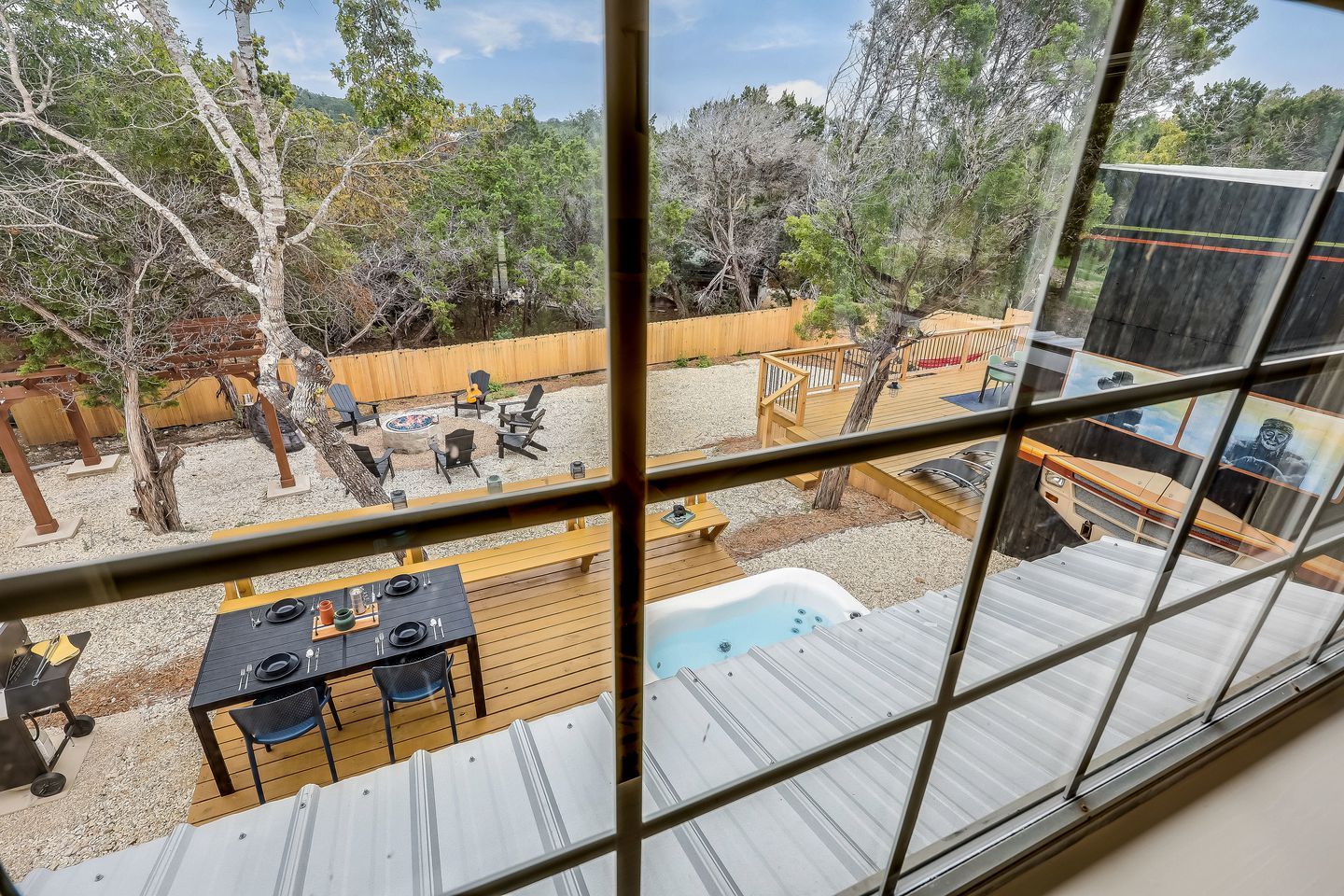 A view through a window of a backyard with a hot tub, outdoor seating, and a wooden deck.
